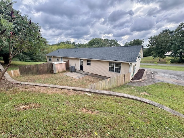 rear view of property featuring central air condition unit, a lawn, a patio area, and fence