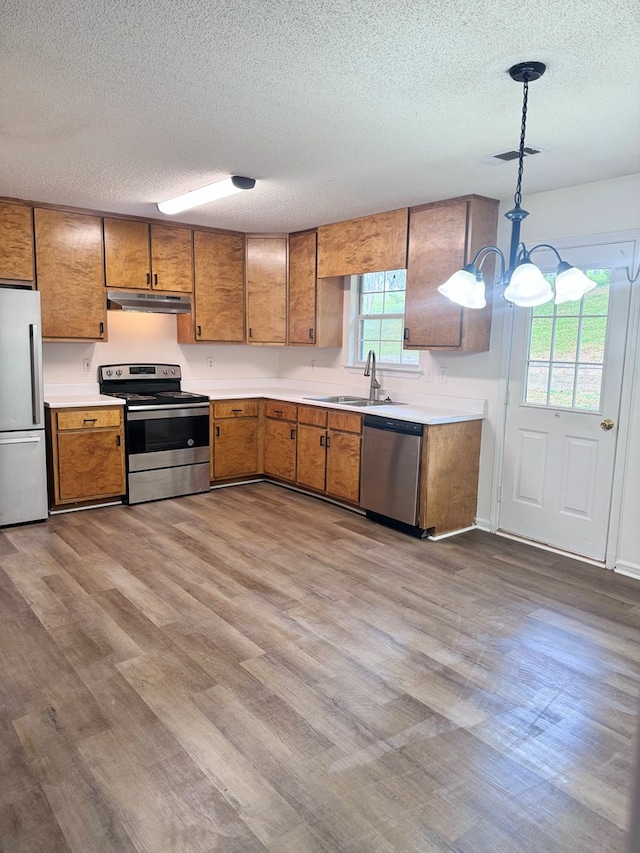 kitchen featuring under cabinet range hood, light countertops, brown cabinetry, stainless steel appliances, and a sink