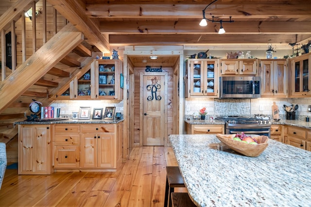 kitchen with decorative backsplash, appliances with stainless steel finishes, light wood-type flooring, and light stone counters