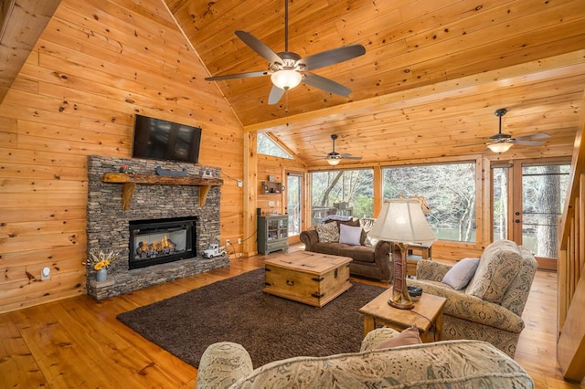 living room featuring a stone fireplace, light hardwood / wood-style floors, lofted ceiling, wooden walls, and wood ceiling