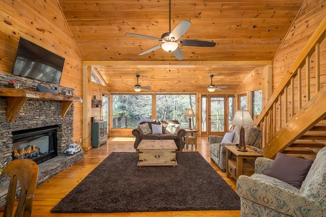 living room featuring vaulted ceiling, wooden walls, wooden ceiling, light hardwood / wood-style floors, and a stone fireplace