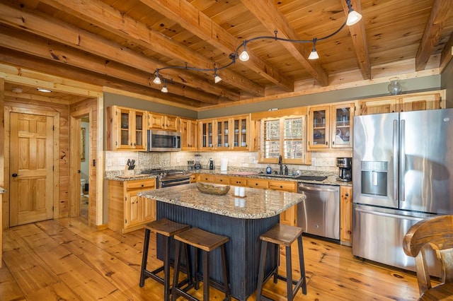 kitchen with light wood-type flooring, appliances with stainless steel finishes, a center island, and light stone counters