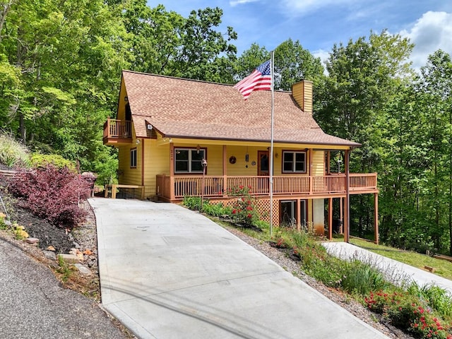 view of front of home featuring a chimney, driveway, a porch, and a shingled roof