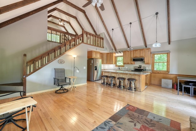 living area with high vaulted ceiling, light wood-type flooring, a ceiling fan, beamed ceiling, and stairs