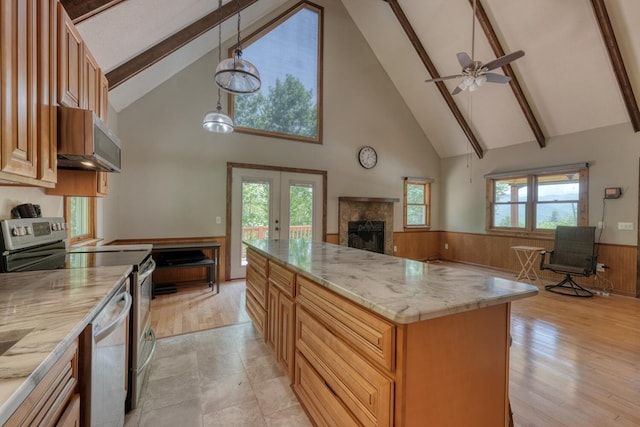 kitchen featuring stainless steel appliances, high vaulted ceiling, a tiled fireplace, wainscoting, and open floor plan