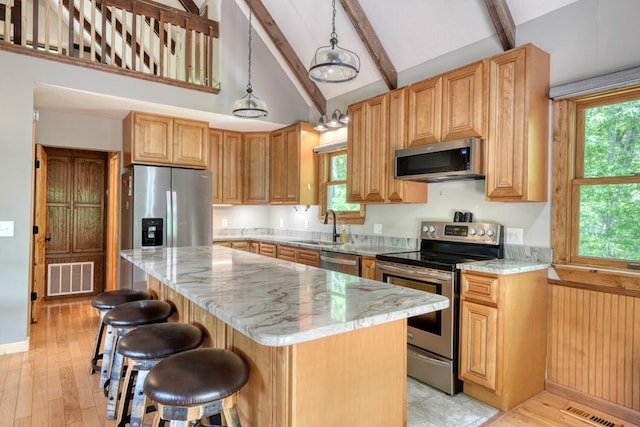 kitchen featuring stainless steel appliances, beam ceiling, a sink, a kitchen island, and a breakfast bar area
