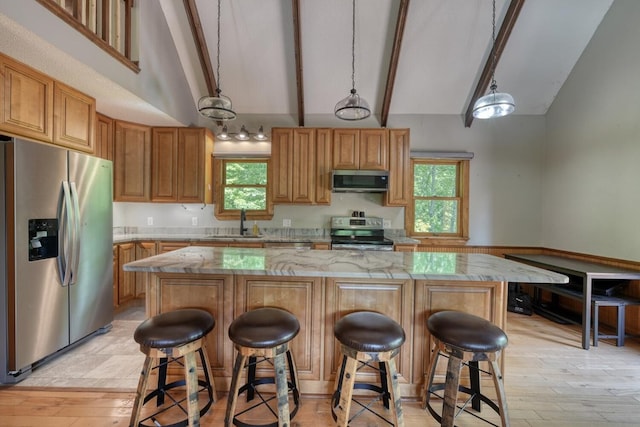 kitchen with appliances with stainless steel finishes, beam ceiling, a center island, a sink, and light stone counters