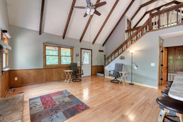 living room with high vaulted ceiling, wood-type flooring, a ceiling fan, a wainscoted wall, and stairs