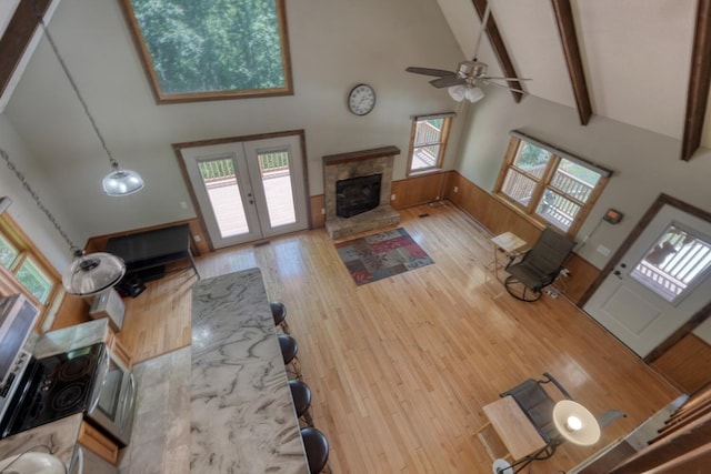 living room with a fireplace, high vaulted ceiling, a ceiling fan, beam ceiling, and wood finished floors