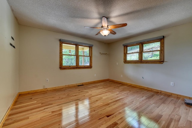 empty room featuring plenty of natural light, light wood-type flooring, ceiling fan, and a textured ceiling