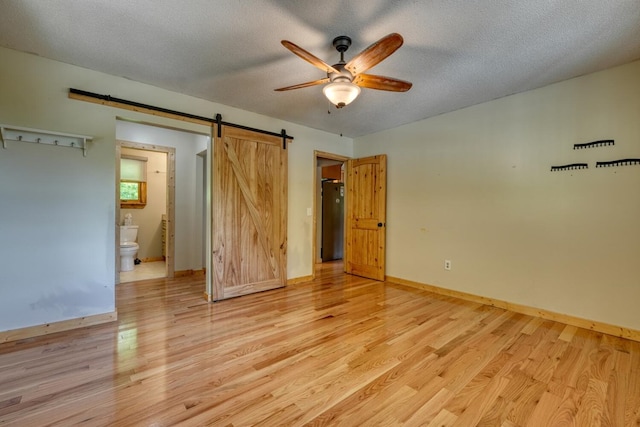 unfurnished bedroom featuring light wood-style floors, a barn door, baseboards, ensuite bathroom, and a textured ceiling