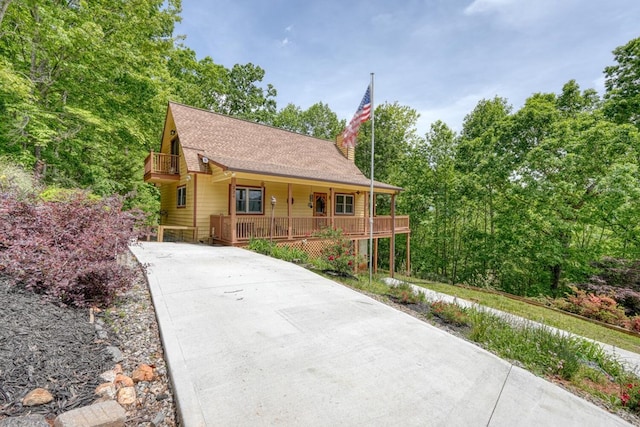rustic home featuring covered porch, concrete driveway, a shingled roof, and a balcony