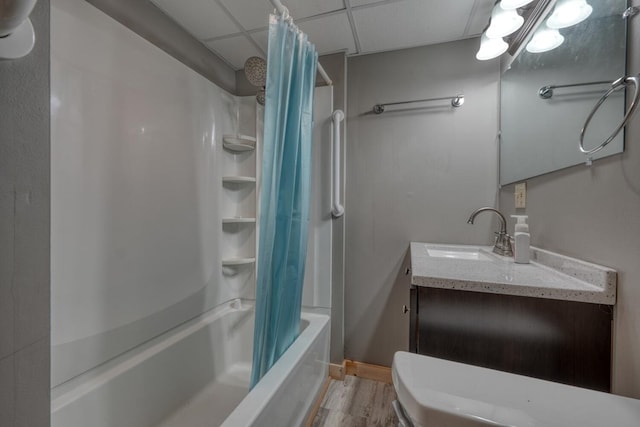 bathroom with a drop ceiling, wood finished floors, shower / bathtub combination with curtain, and vanity