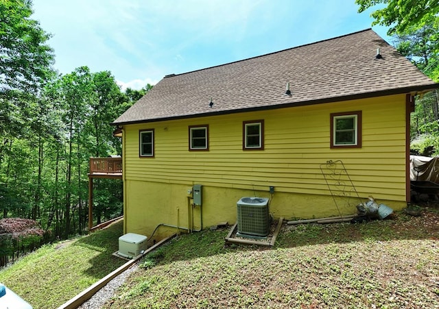 rear view of property featuring cooling unit and a shingled roof