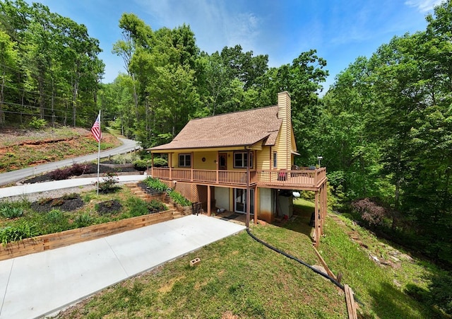view of front of property with a deck, a chimney, stairway, a wooded view, and a front lawn