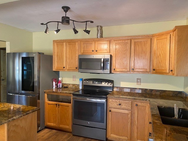 kitchen with dark wood-style floors, dark stone counters, appliances with stainless steel finishes, and a sink
