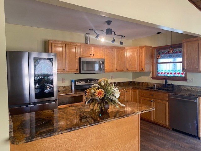 kitchen with decorative light fixtures, a sink, dark stone counters, appliances with stainless steel finishes, and dark wood-style floors