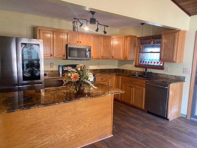 kitchen with dark stone countertops, a sink, stainless steel appliances, dark wood finished floors, and decorative light fixtures