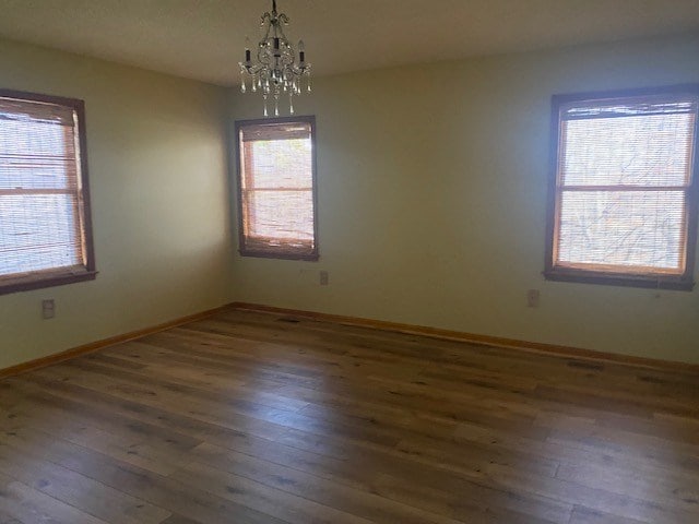 empty room featuring baseboards, hardwood / wood-style floors, a healthy amount of sunlight, and an inviting chandelier