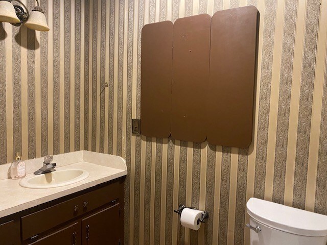 half bathroom with toilet, vanity, and wallpapered walls