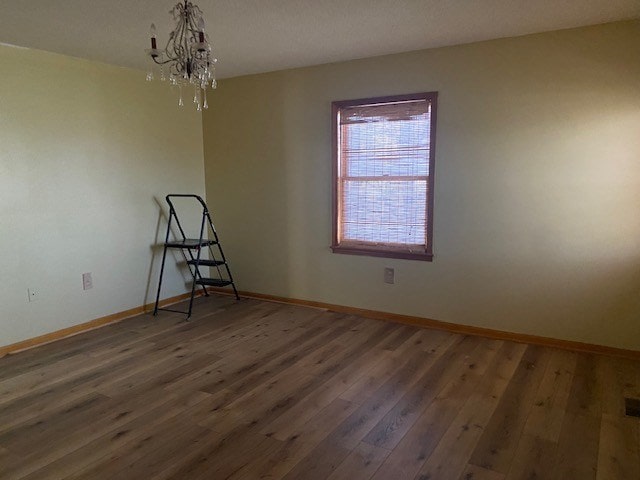 unfurnished room featuring baseboards, a notable chandelier, and wood finished floors