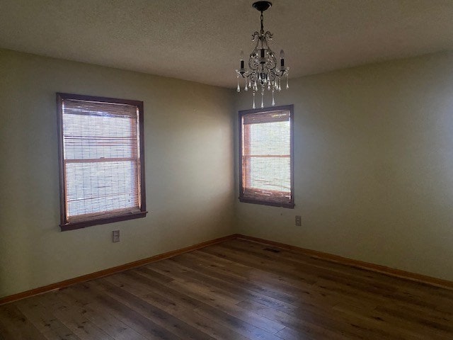 spare room featuring a chandelier, hardwood / wood-style flooring, and baseboards