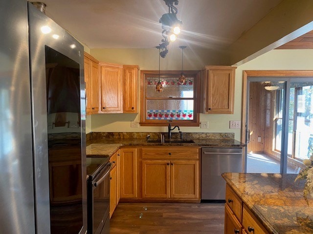 kitchen featuring a sink, stainless steel appliances, dark wood finished floors, and dark stone counters