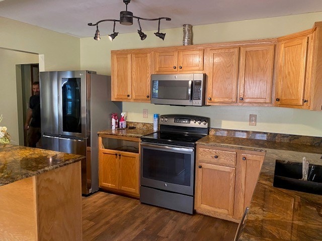 kitchen with a sink, dark wood-style flooring, dark stone counters, and appliances with stainless steel finishes