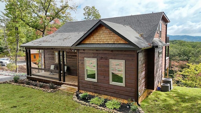 back of house featuring cooling unit, a shingled roof, a mountain view, and a lawn