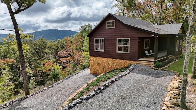 view of front facade with driveway, a mountain view, a porch, and roof with shingles