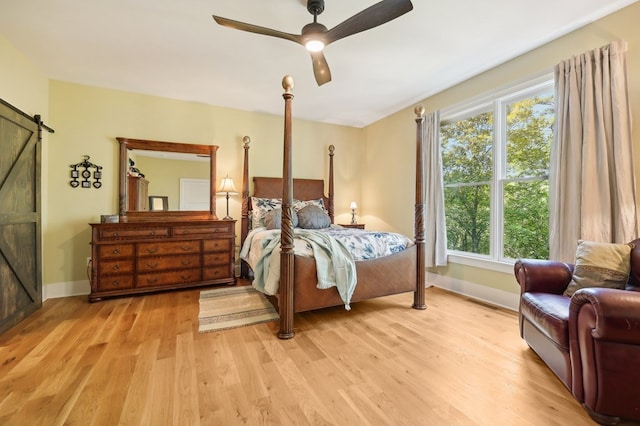 bedroom featuring a barn door, ceiling fan, multiple windows, and light hardwood / wood-style flooring