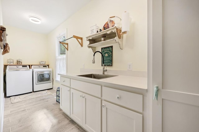 clothes washing area with light wood-type flooring, sink, independent washer and dryer, and cabinets