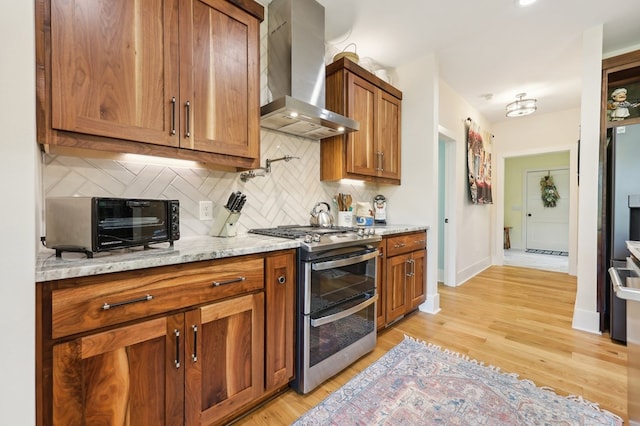 kitchen with range with two ovens, light hardwood / wood-style floors, wall chimney range hood, and tasteful backsplash