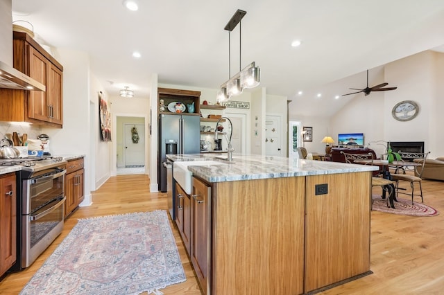 kitchen with an island with sink, light hardwood / wood-style flooring, appliances with stainless steel finishes, light stone countertops, and ceiling fan