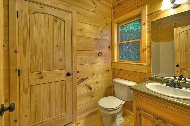bathroom featuring wooden walls, toilet, vanity, and wood finished floors