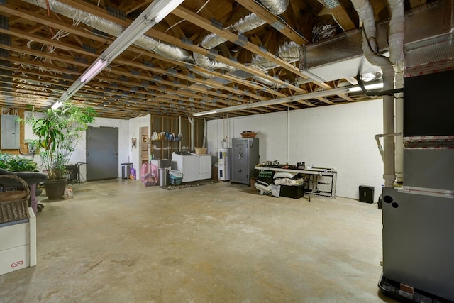 unfinished below grade area featuring washing machine and clothes dryer, water heater, electric panel, heating unit, and concrete block wall