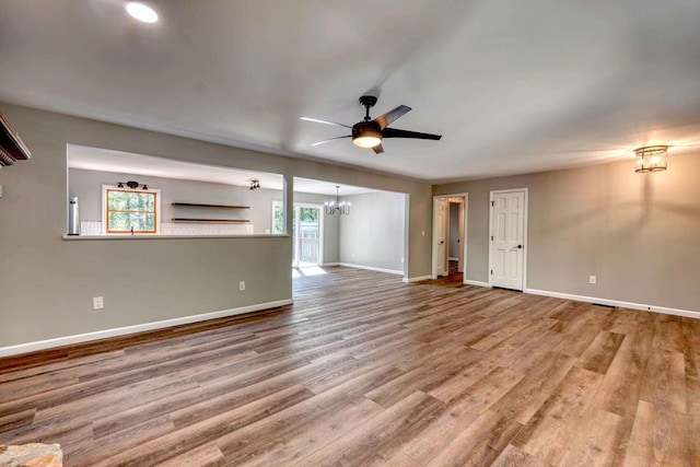 unfurnished living room with ceiling fan with notable chandelier, a wealth of natural light, and wood-type flooring