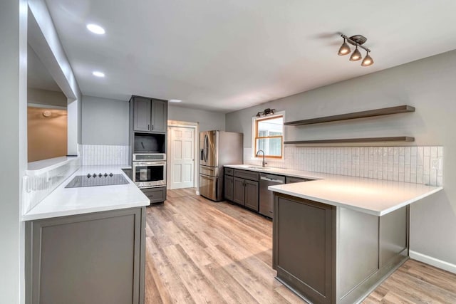 kitchen with sink, appliances with stainless steel finishes, tasteful backsplash, light hardwood / wood-style floors, and kitchen peninsula