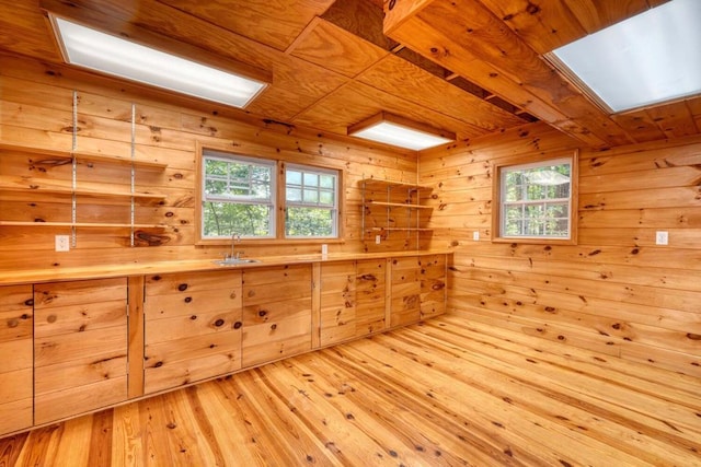 interior space featuring a skylight, sink, wooden walls, and light hardwood / wood-style flooring