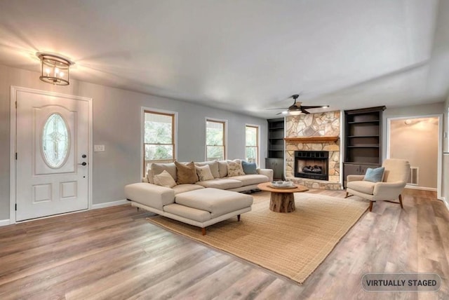 living room featuring hardwood / wood-style flooring, ceiling fan, a stone fireplace, and built in shelves