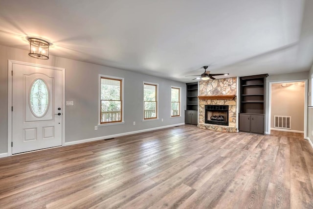 unfurnished living room featuring hardwood / wood-style flooring, ceiling fan, a stone fireplace, and built in features