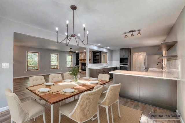 dining area featuring ceiling fan, a stone fireplace, sink, and dark hardwood / wood-style flooring