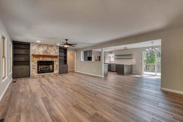 unfurnished living room with wood-type flooring, ceiling fan with notable chandelier, a fireplace, and built in shelves