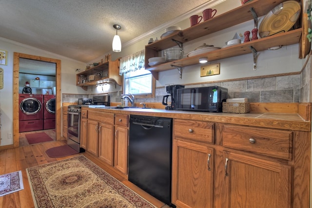 kitchen featuring washing machine and clothes dryer, sink, light hardwood / wood-style flooring, decorative light fixtures, and black appliances