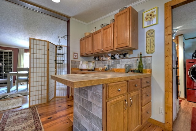 kitchen featuring tasteful backsplash, light hardwood / wood-style flooring, washer / clothes dryer, crown molding, and a textured ceiling