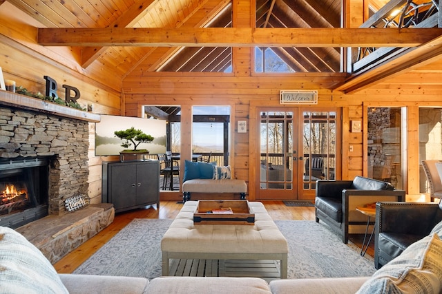 living room featuring beam ceiling, wooden walls, a stone fireplace, french doors, and light wood-type flooring