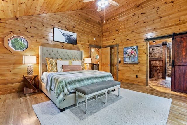 bedroom featuring wood ceiling, ceiling fan, wooden walls, a barn door, and light wood-type flooring