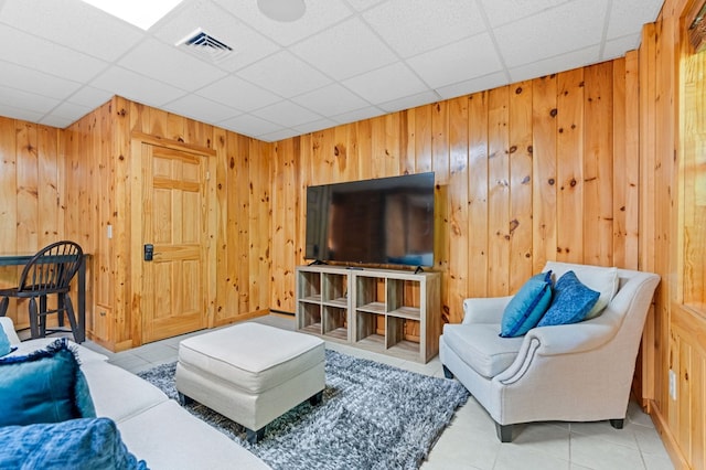 living room featuring wooden walls, light tile patterned floors, and a drop ceiling