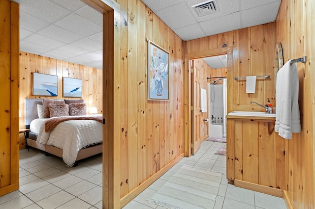 interior space featuring a drop ceiling, connected bathroom, sink, and wood walls