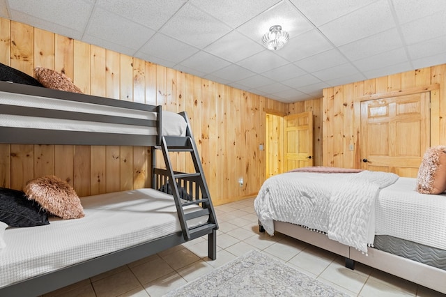 tiled bedroom featuring a drop ceiling and wood walls